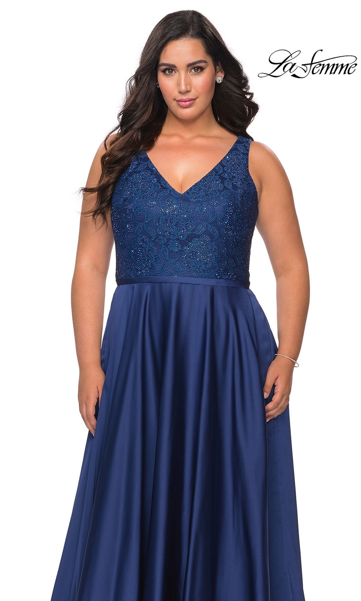 A plus-size person wears a Long Plus-Size Prom Dress: La Femme 29004, a navy blue formal gown with a V-neckline, a rhinestone-embellished lace bodice, and a smooth satin A-line skirt.